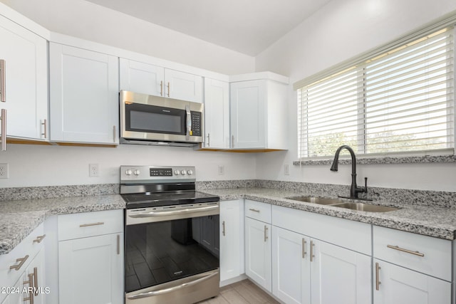 kitchen with light stone counters, white cabinets, sink, stainless steel appliances, and light wood-type flooring