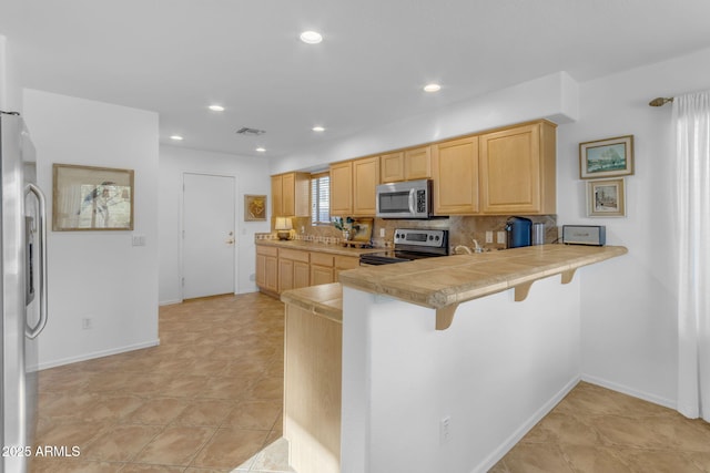 kitchen with a kitchen bar, light brown cabinets, kitchen peninsula, stainless steel appliances, and decorative backsplash