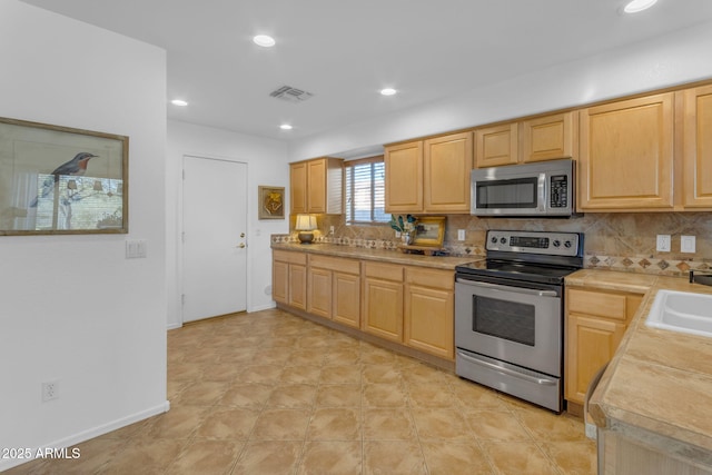 kitchen with stainless steel appliances, sink, light brown cabinetry, and decorative backsplash