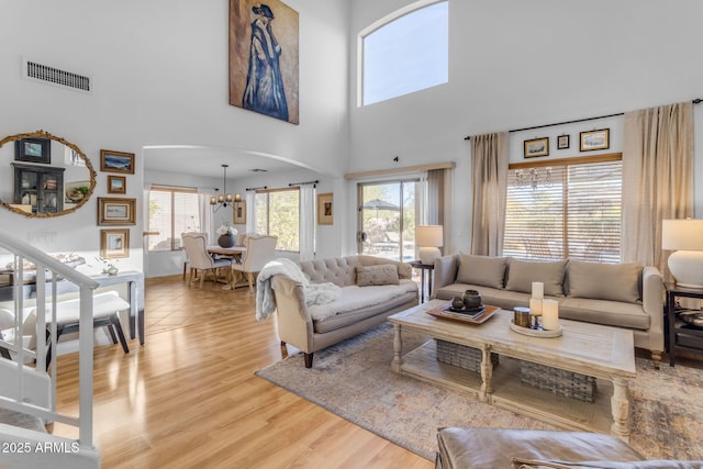 living room with a towering ceiling, a chandelier, and light wood-type flooring