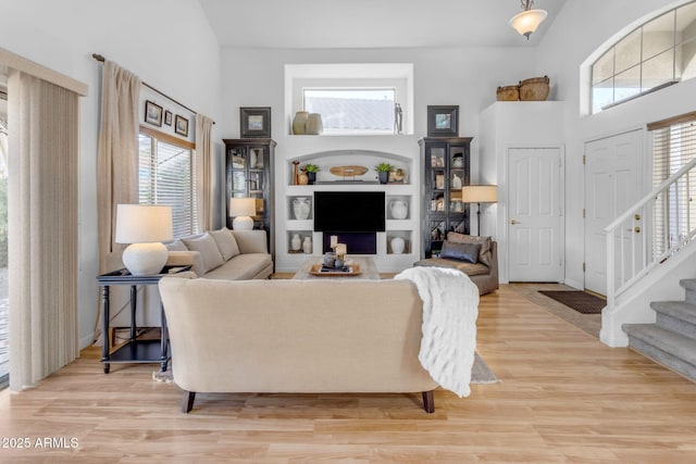 living room with built in shelves, wood-type flooring, and a towering ceiling