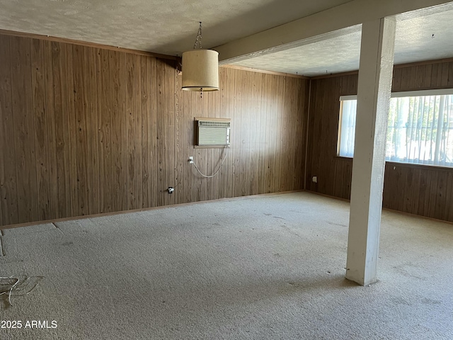 empty room featuring a wall mounted AC, carpet flooring, wooden walls, a textured ceiling, and baseboards