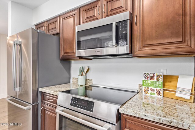 2015 E Southern Ave Unit 16, Tempe, AZ 85282 - kitchen with appliances with stainless steel finishes, brown cabinetry, light stone counters, and light wood-style floors