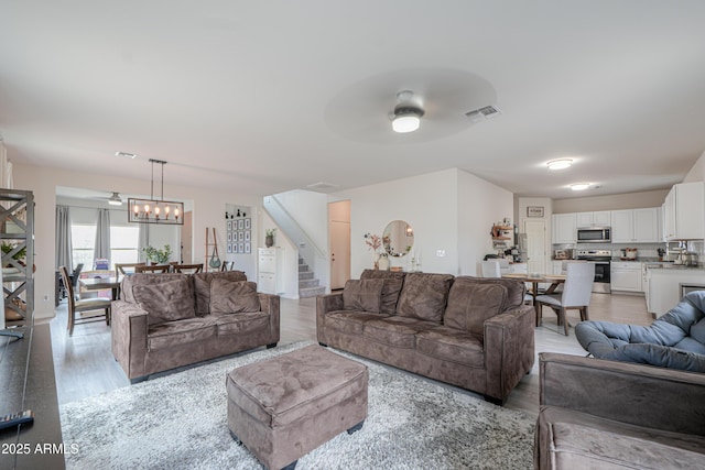 living room with light wood-type flooring, visible vents, stairway, and a ceiling fan