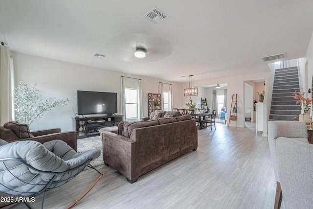 living room featuring stairs, visible vents, light wood-type flooring, and a ceiling fan