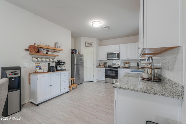 kitchen featuring light wood-type flooring, stainless steel appliances, visible vents, white cabinets, and decorative backsplash