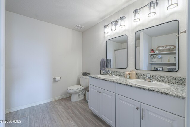 bathroom with toilet, wood finished floors, baseboards, and a sink