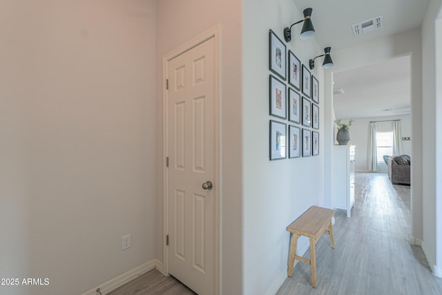 corridor featuring baseboards, visible vents, and light wood-type flooring