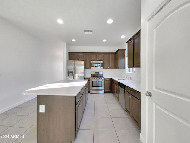 kitchen with light tile patterned flooring, stainless steel appliances, dark brown cabinets, sink, and a center island