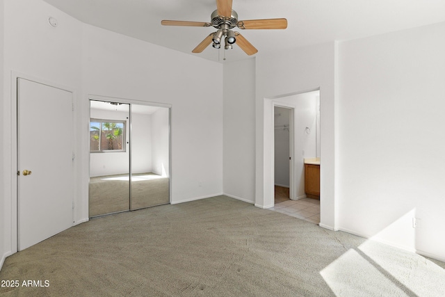 unfurnished bedroom featuring a ceiling fan, a closet, light carpet, and ensuite bathroom