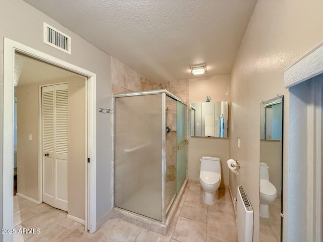 bathroom featuring a textured ceiling, radiator heating unit, tile patterned flooring, a shower with door, and toilet