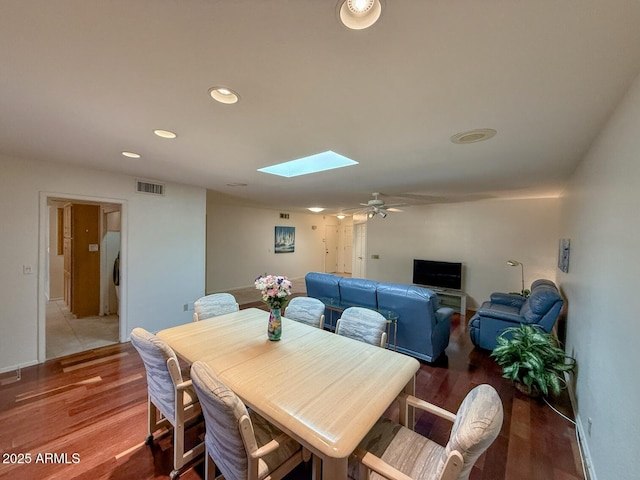 dining space with ceiling fan, hardwood / wood-style floors, and a skylight