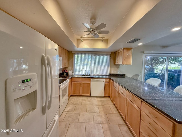 kitchen featuring white appliances, a tray ceiling, dark stone countertops, kitchen peninsula, and light tile patterned flooring