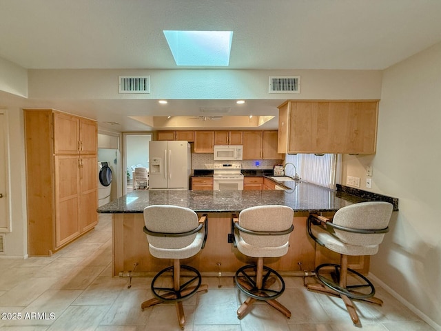 kitchen with white appliances, a kitchen bar, a skylight, dark stone countertops, and sink