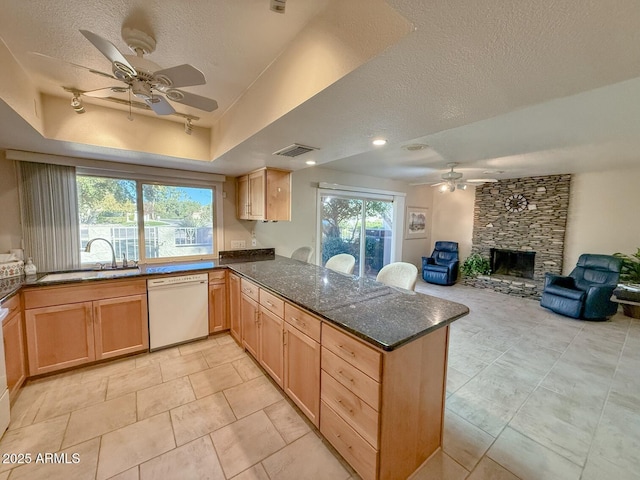 kitchen featuring kitchen peninsula, dishwasher, sink, a tray ceiling, and a fireplace