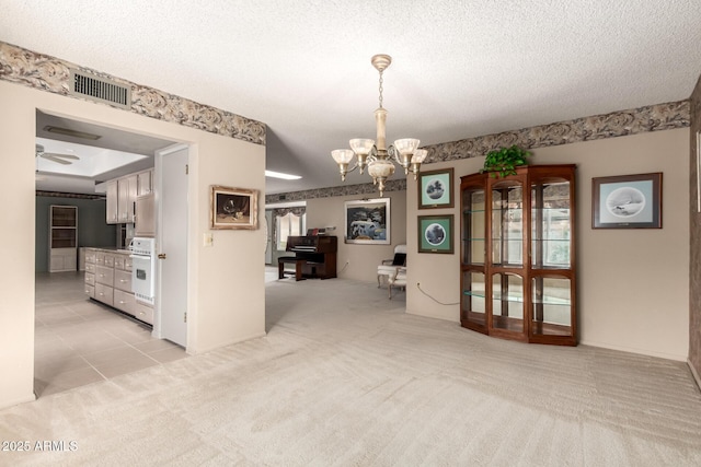 unfurnished dining area with light carpet, a textured ceiling, ceiling fan with notable chandelier, and visible vents