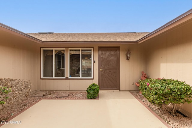 view of exterior entry featuring a patio and roof with shingles