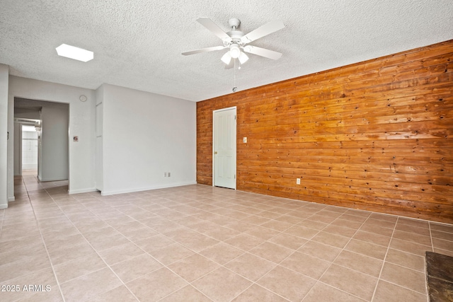 unfurnished room featuring ceiling fan, a textured ceiling, wood walls, baseboards, and light tile patterned flooring
