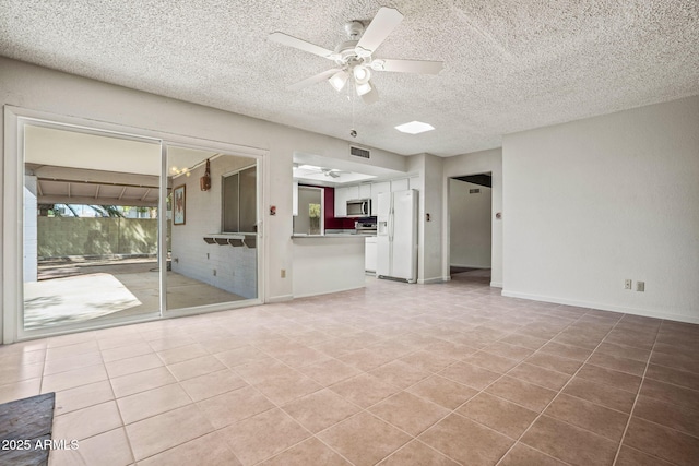 unfurnished living room featuring ceiling fan, a textured ceiling, visible vents, light tile patterned floors, and baseboards