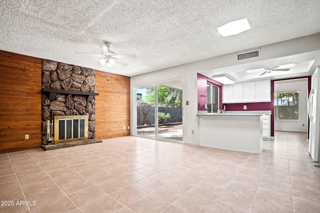 unfurnished living room with light tile patterned floors, a ceiling fan, wood walls, and visible vents