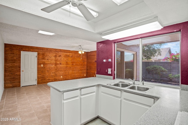 kitchen with white cabinets, ceiling fan, a sink, wood walls, and a peninsula