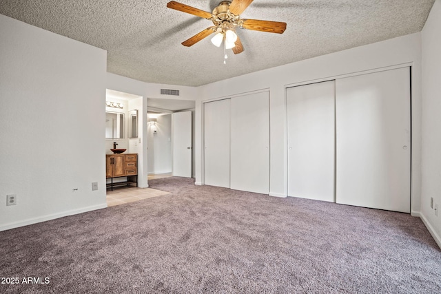 unfurnished bedroom featuring multiple closets, a textured ceiling, carpet floors, and visible vents