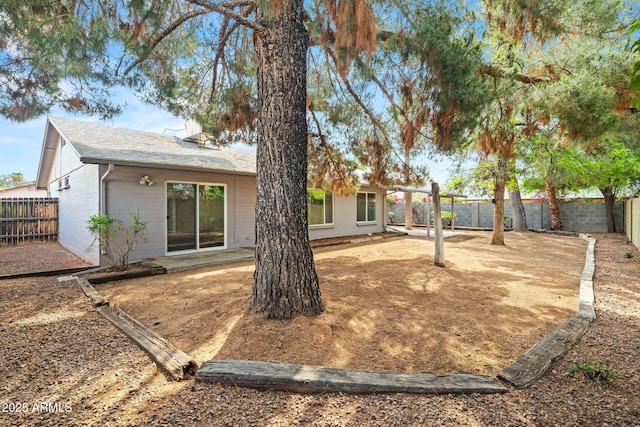 back of house with a fenced backyard, a patio, roof with shingles, and brick siding