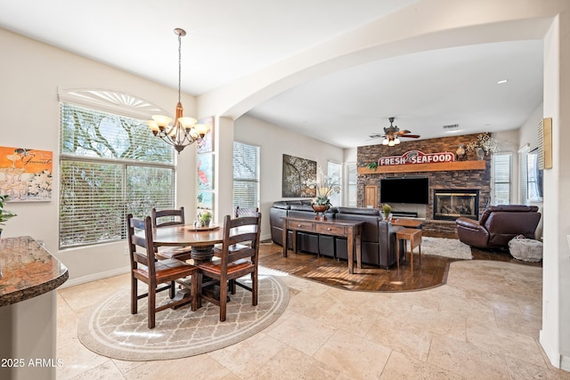 dining area featuring a stone fireplace and ceiling fan with notable chandelier