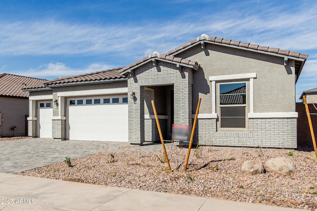 view of front of property featuring a garage, brick siding, a tile roof, decorative driveway, and stucco siding