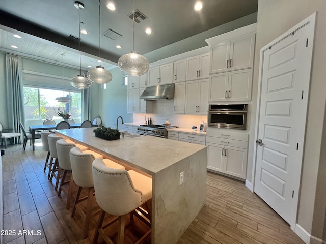 kitchen with visible vents, light wood-style flooring, decorative backsplash, appliances with stainless steel finishes, and under cabinet range hood