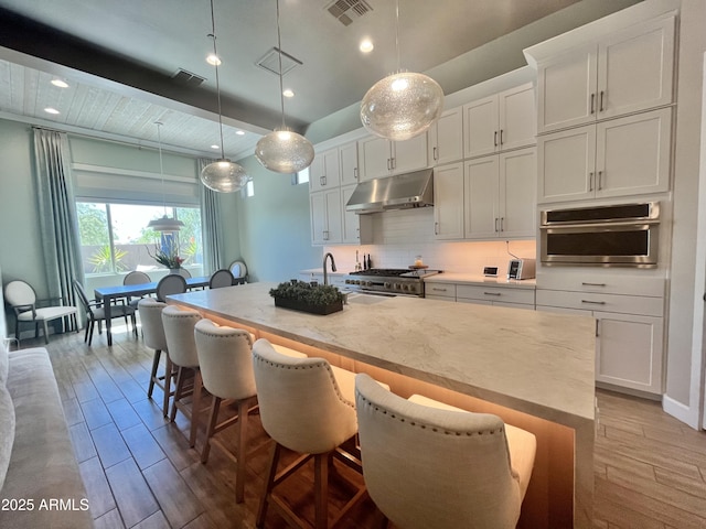 kitchen featuring light wood finished floors, visible vents, decorative backsplash, appliances with stainless steel finishes, and under cabinet range hood