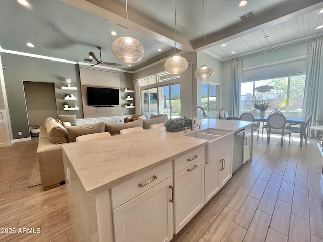 kitchen with dishwasher, wood finish floors, a sink, and a center island with sink