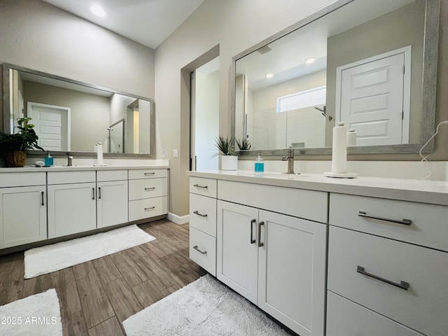 full bath featuring a stall shower, two vanities, a sink, and wood finished floors