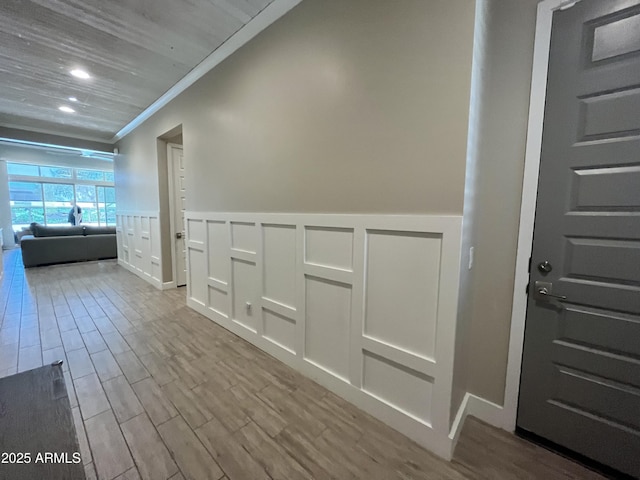 hallway featuring a decorative wall, a wainscoted wall, recessed lighting, wood finished floors, and ornamental molding