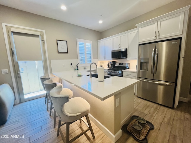 kitchen featuring stainless steel appliances, light wood finished floors, a kitchen bar, and a sink