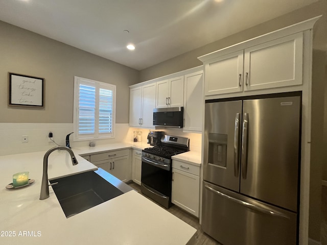 kitchen featuring white cabinets, appliances with stainless steel finishes, light countertops, a sink, and recessed lighting