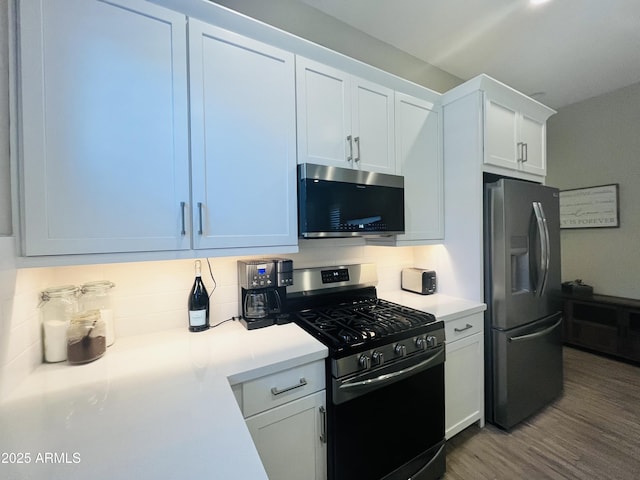 kitchen with tasteful backsplash, white cabinets, appliances with stainless steel finishes, wood finished floors, and light countertops