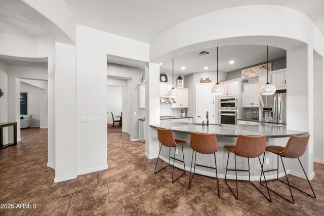 20546 W Summit Pl, Buckeye, AZ 85396 - kitchen featuring stainless steel appliances, white cabinets, a sink, a breakfast bar area, and tasteful backsplash