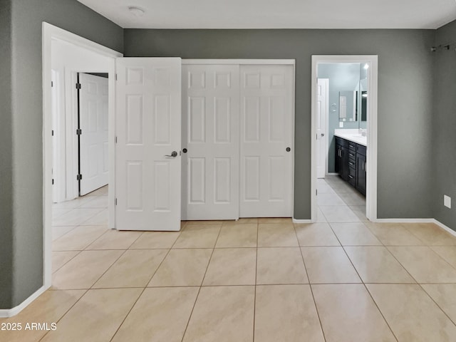 unfurnished bedroom with ensuite bathroom, a closet, and light tile patterned floors