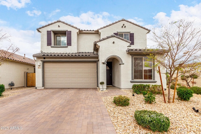 mediterranean / spanish-style house with an attached garage, stucco siding, decorative driveway, and a tiled roof