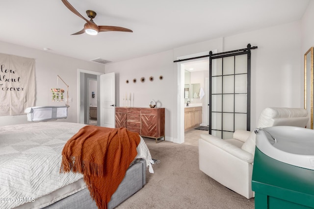 bedroom featuring visible vents, ensuite bathroom, a barn door, light carpet, and ceiling fan