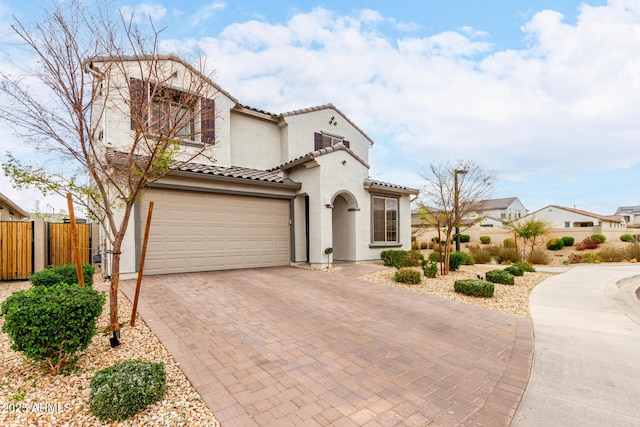 mediterranean / spanish-style home with decorative driveway, stucco siding, an attached garage, fence, and a tiled roof