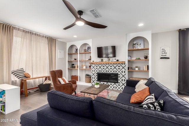 living area with visible vents, a ceiling fan, a tile fireplace, wood finished floors, and built in shelves