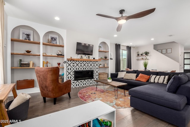 living room with built in features, a tile fireplace, recessed lighting, and wood finished floors