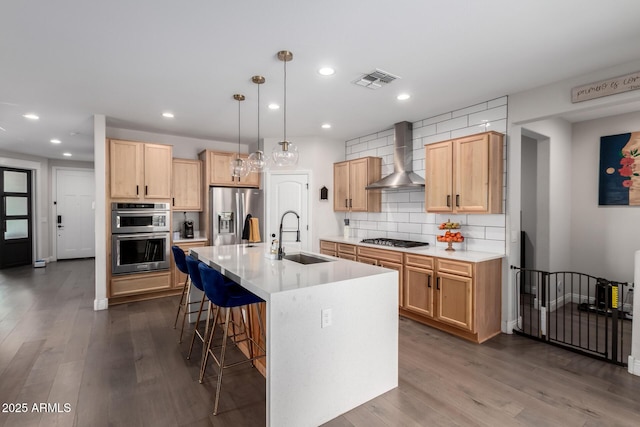 kitchen featuring a breakfast bar area, stainless steel appliances, visible vents, a sink, and wall chimney range hood