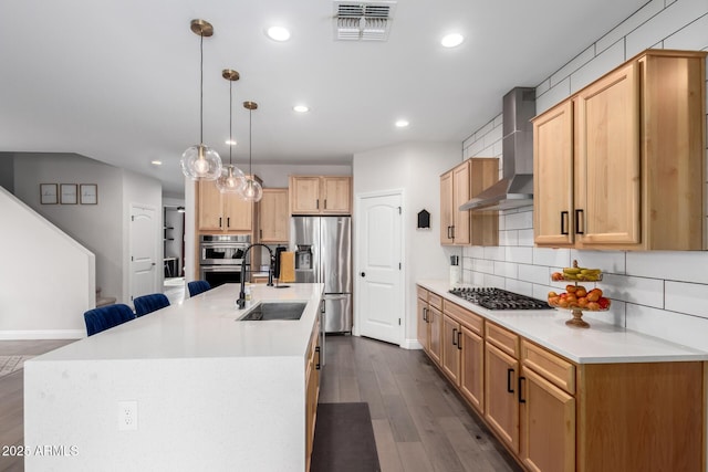 kitchen featuring stainless steel appliances, a sink, visible vents, wall chimney exhaust hood, and tasteful backsplash