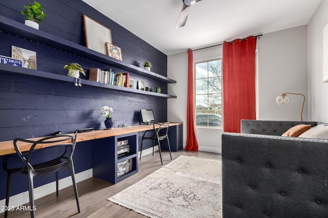 home office featuring light wood finished floors, a ceiling fan, built in study area, wooden walls, and baseboards