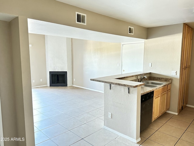 kitchen featuring a large fireplace, sink, dishwashing machine, a kitchen bar, and light tile patterned floors