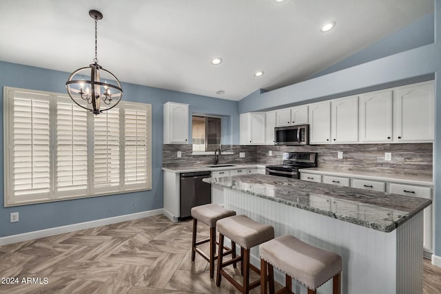 kitchen featuring decorative light fixtures, stainless steel appliances, white cabinetry, a sink, and a kitchen island