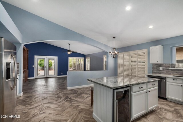 kitchen featuring tasteful backsplash, appliances with stainless steel finishes, white cabinets, a kitchen island, and a towering ceiling